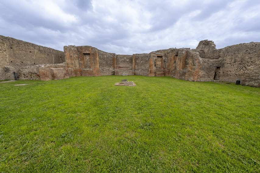 Rovine del Santuario dei Lari Pubblici a Pompei con prato verde e struttura muraria